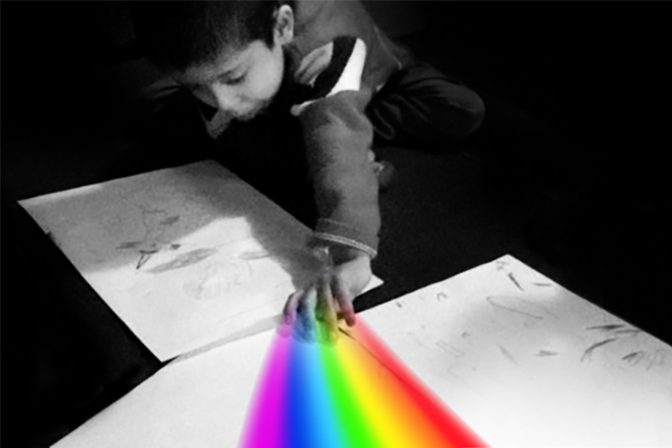 Black background with boy creating a rainbow on white paper with his fingers